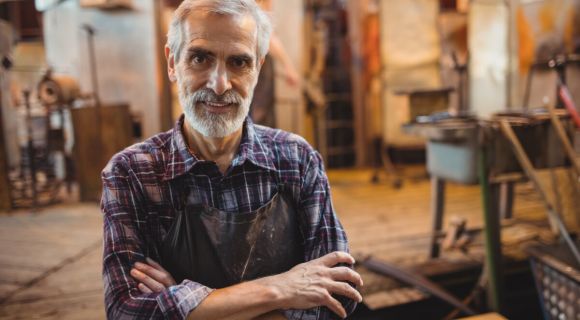 Portrait of glassblower standing with arms crossed at glassblowing factory
