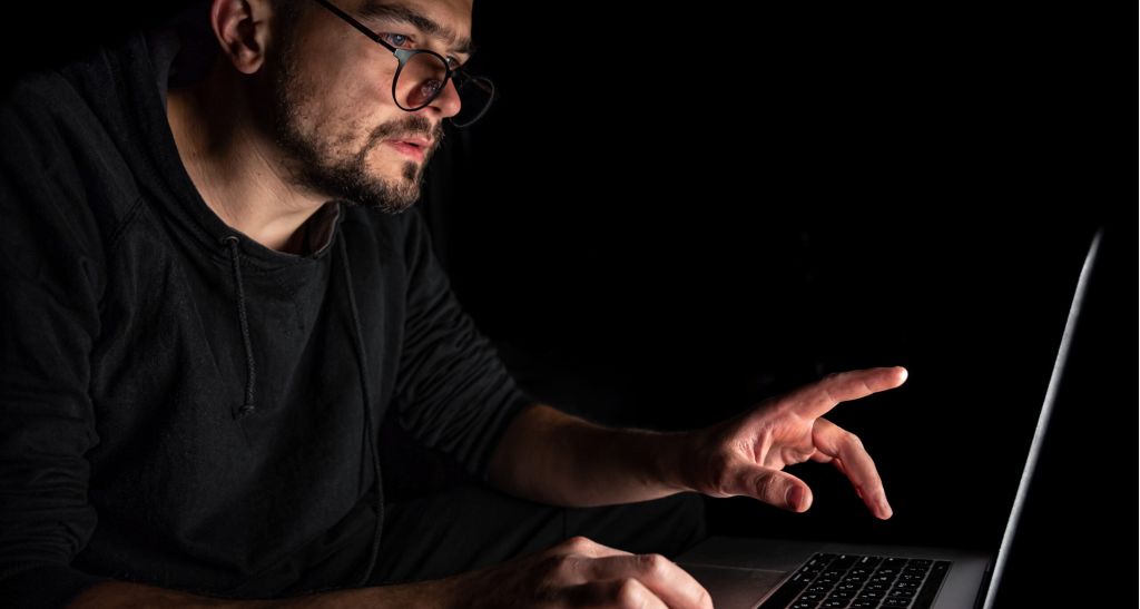 man with glasses works laptop dark