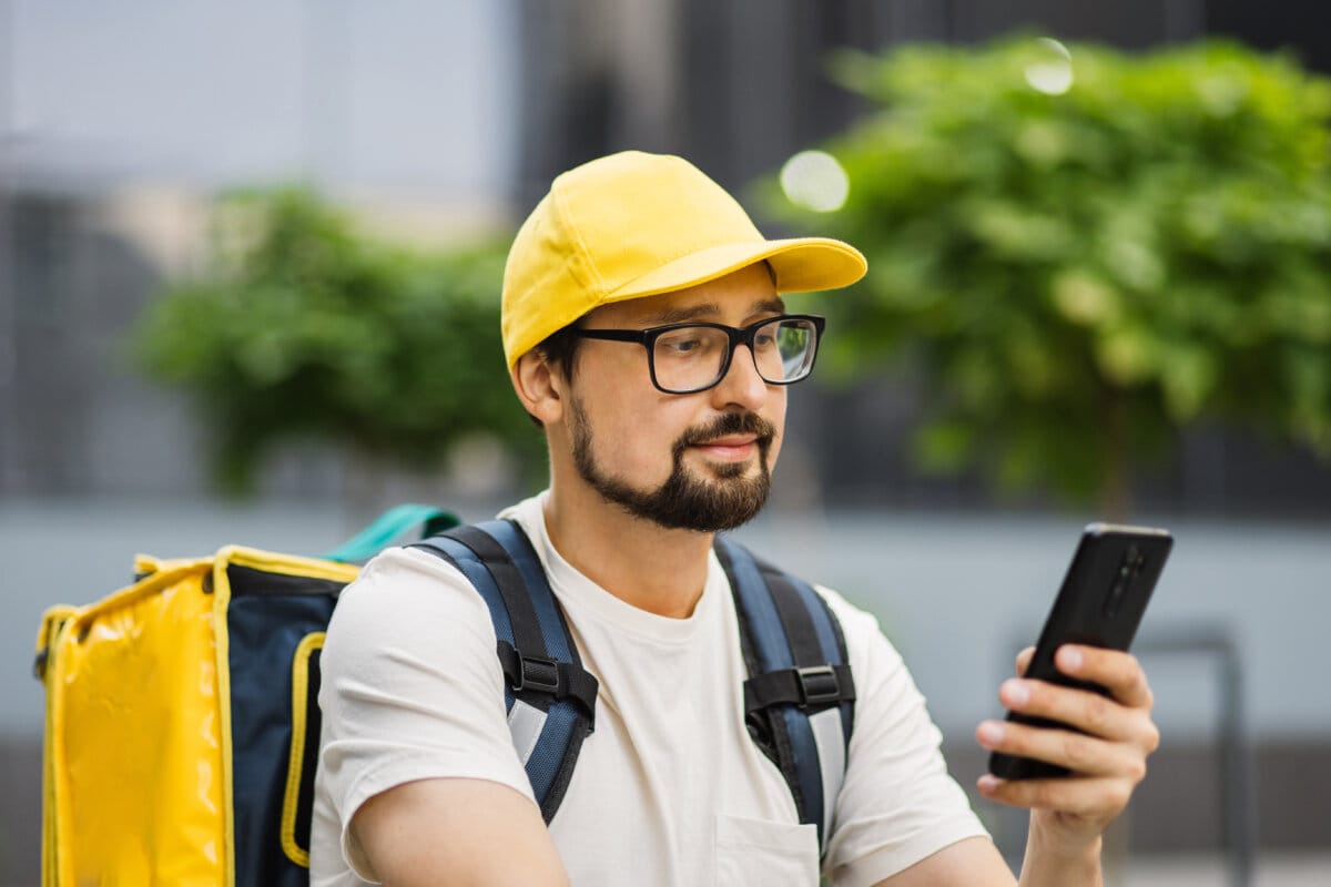 Caucasian man courier of food delivery with big thermal backpack on his back talking on smartphone