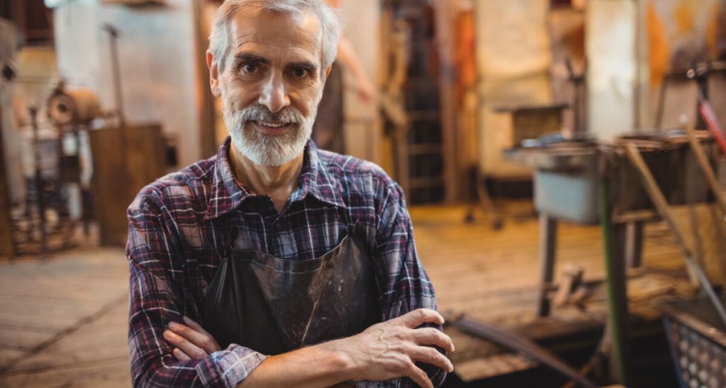 Portrait of glassblower standing with arms crossed at glassblowing factory