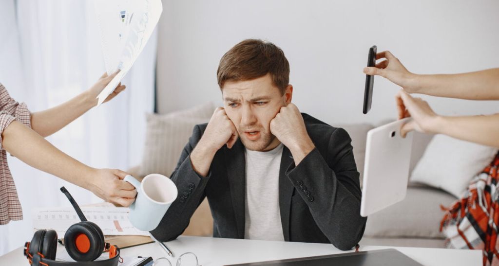 Many hands reach out to a man with various objects